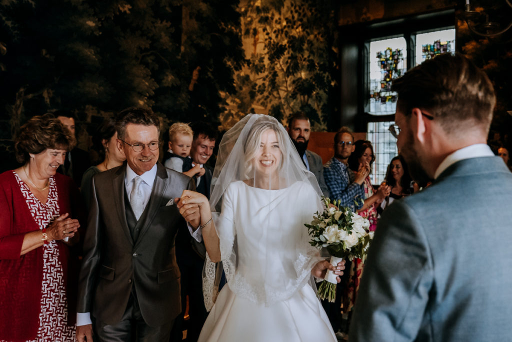 Bruid wordt door haar vader binnengebracht in de trouwzaal van het stadhuis van Gouda. Bruid lacht naar bruidegom