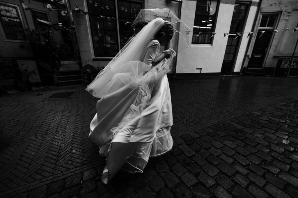 Bruid en bruidegom rennen met paraplu door de regen naar de SintJan in Gouda