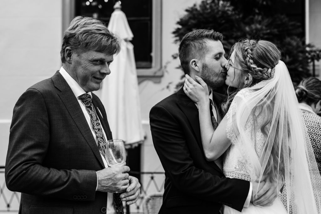 Bruid en bruidegom kussen, vader van de bruidegom kijkt weg