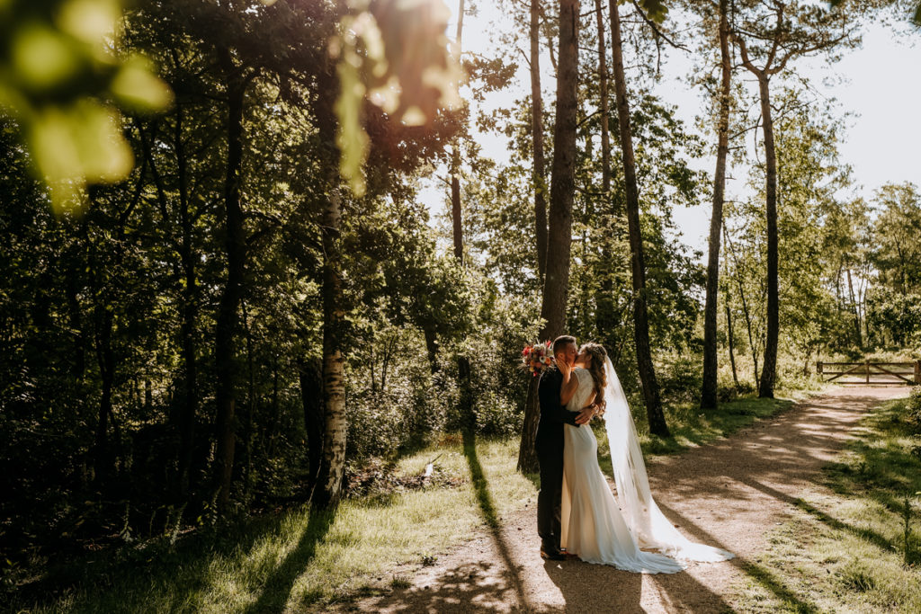 Bruidspaar kust elkaar in het bos met tegenlicht