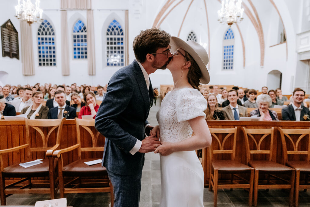 Bruidspaar geeft elkaar een kus voorin de kerk