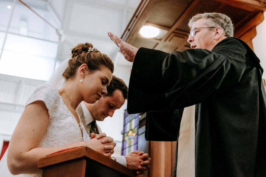 Bruid en bruidegom knielen in de kerk en de dominee zegent hen
