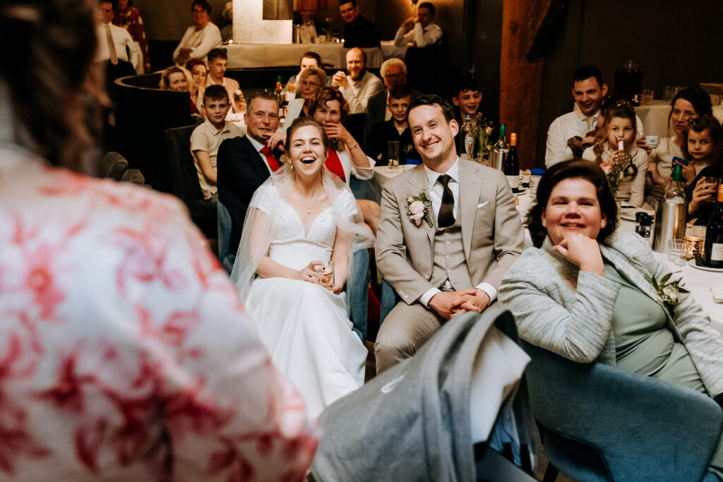 Bruidspaar moet lachen om een speech van een vriendin, alle gasten lachen mee