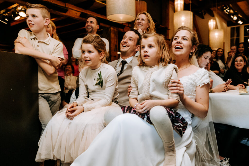 Bruidspaar met veel kinderen op schoot luistert naar sketch en moet lachen
