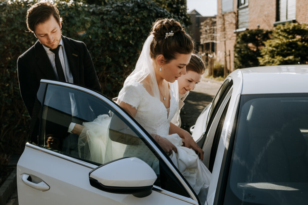 Bruid stapt in de auto met mooi tegenlicht