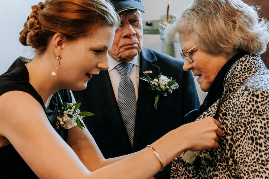 Zus van de bruid, met corsage, speldt corsage op bij oma