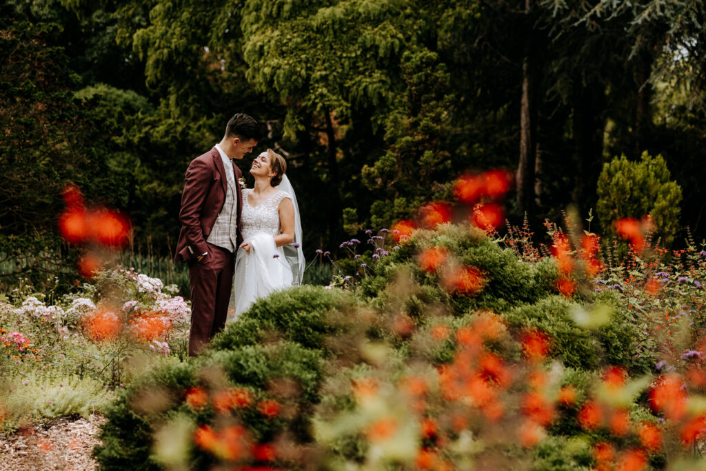 Bruidspaar staat in park tussen rode bloemen
