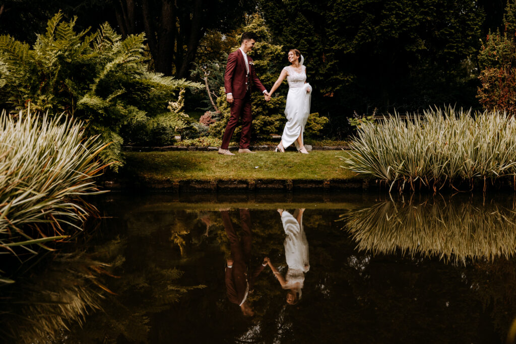 Bruid leidt bruidegom aan de hand langs vijver en hun spiegelbeeld is te zien
