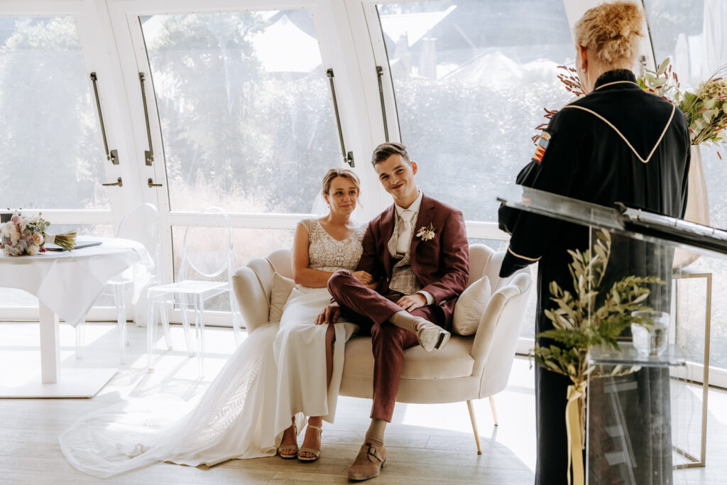 Bruid en bruidegom zitten te luisteren naar de trouwambtenaar