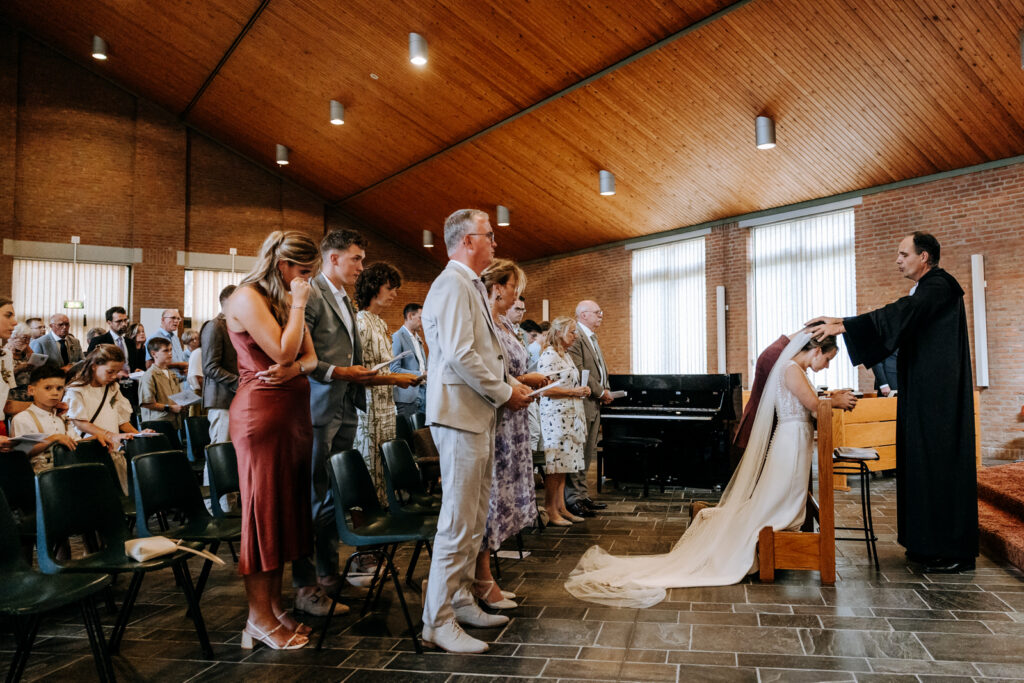 Bruidspaar in de kerk knielt neer en wordt gezegend door de dominee