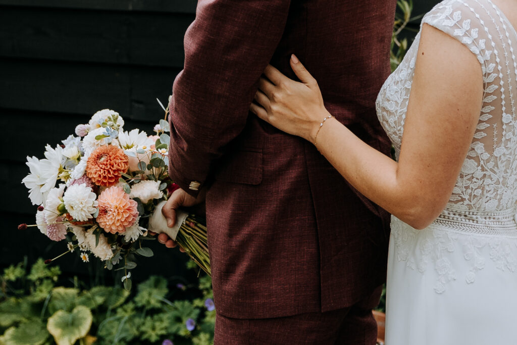 Hand van bruid op rug van bruidegom vlak voor de first look