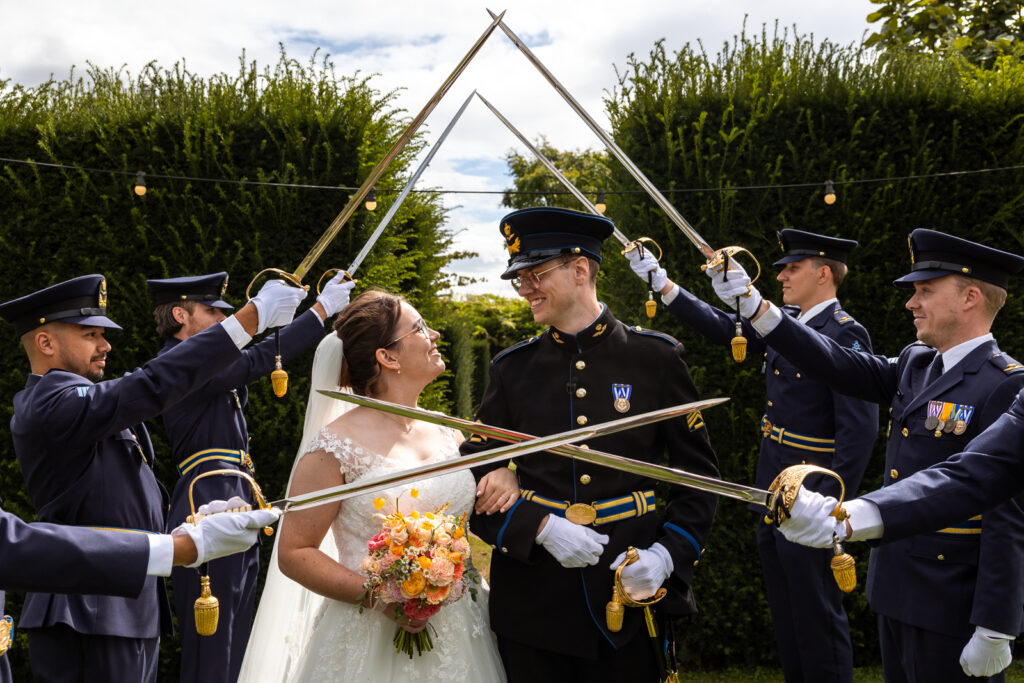 Bruid en bruidegom kijken elkaar lachend aan terwijl ze door de sabelwacht lopen