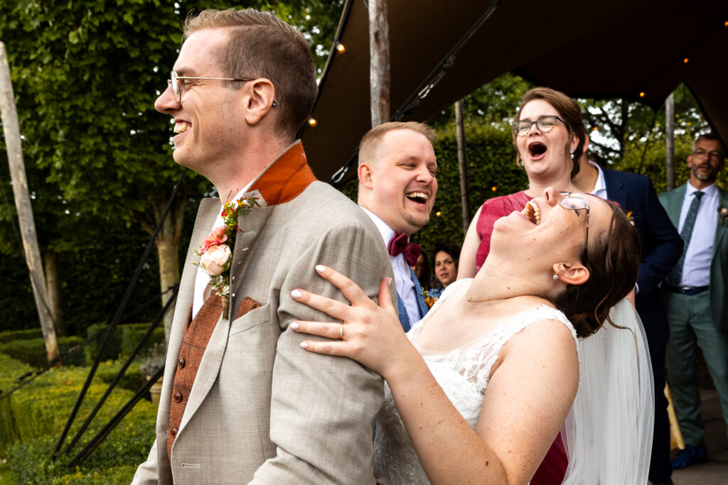 Bruid en gasten lachen heel hard om de tekst in de kraag van de bruidegom