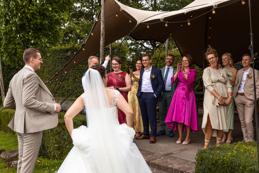 Een kleurige, vrolijke foto van de bruiloftsgasten die hard lachen en applaudisseren om het pak van de bruidegom