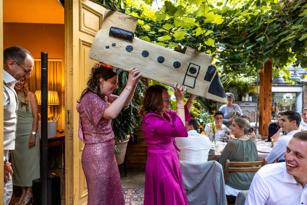 Twee vrolijke, kleurrijke bruiloftsgasten dragen een zelfgemaakte Chinook door de dinerzaal