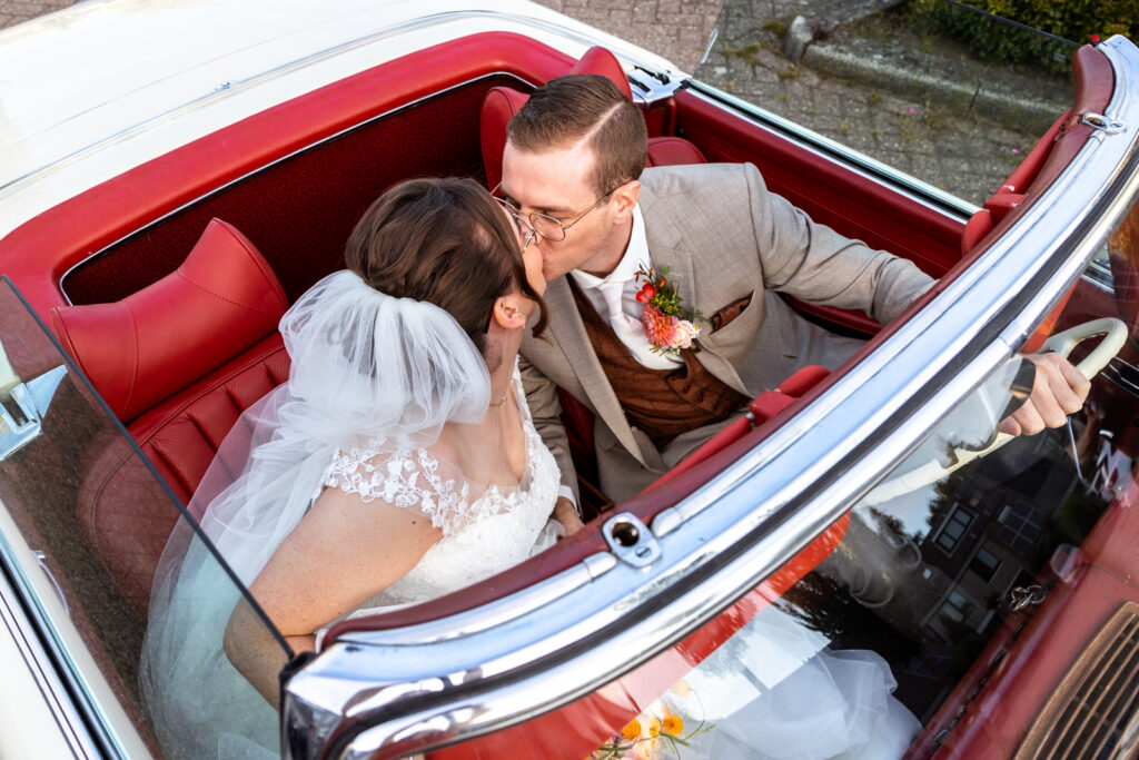 Bruidspaar kust elkaar in hun trouwauto met open dak