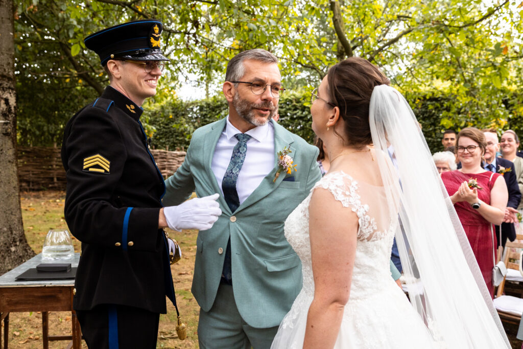 Een persoonlijk moment op deze buitenbruiloft: de vader van de bruid geeft haar weg aan de bruidegom en kijkt haar liefdevol aan
