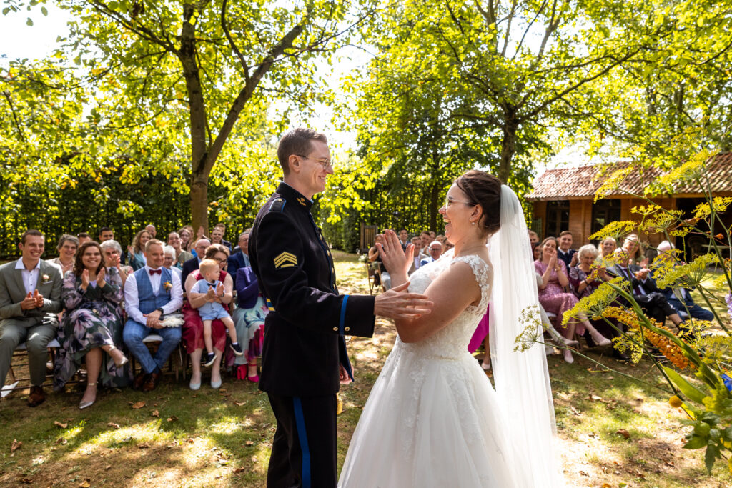Spontane en kleurrijke trouwfoto van bruidspaar tijdens buiten ceremonie in het groen met applaudiserende gasten