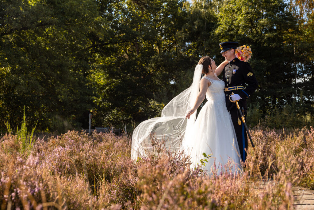 Bruid en bruidegom op de heide, de bruidegom in uniform en de bruid wappert met haar sluier