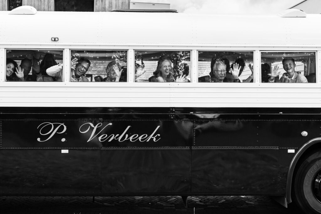 De bruiloftgasten zwaaien vanuit de oldtimer bus